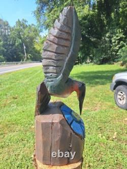 Colibri en bois sculpté à la tronçonneuse unique, en vol stationnaire au-dessus d’une fleur bleue