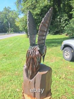 Colibri en bois sculpté à la tronçonneuse unique, en vol stationnaire au-dessus d’une fleur bleue