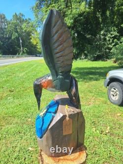 Colibri en bois sculpté à la tronçonneuse unique, en vol stationnaire au-dessus d’une fleur bleue