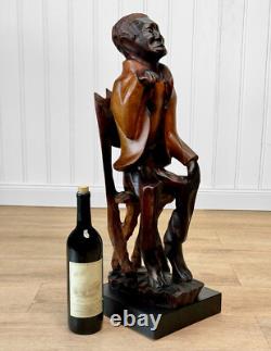 Sculpture en bois sculptée d'un homme africain folklorique vintage assis sur une chaise, grande taille 26 Sculpture en bois sculptée d'un homme africain folklorique vintage assis sur une chaise, grande taille 26